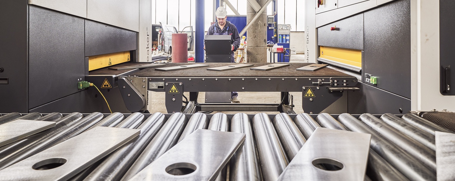 Arbeiter, der Maschinen in einer industriellen Umgebung bedient, mit Metallblechen auf einem Förderband und großen Geräten, die ihn umgeben.